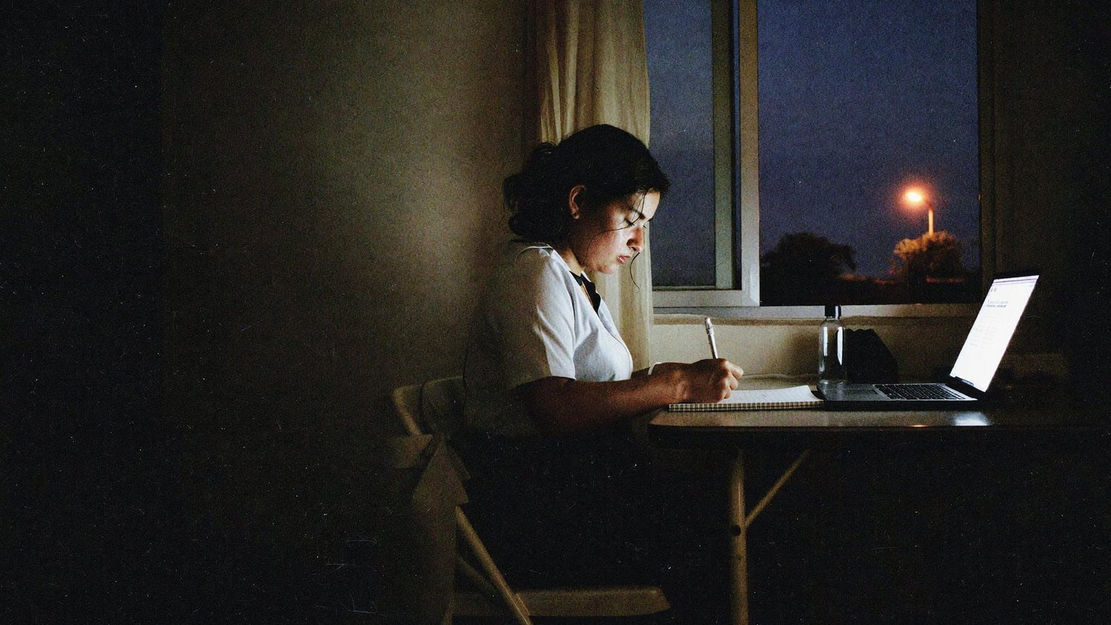 Mesa de estudio de noche con laptop y uniforme de trabajo colgado