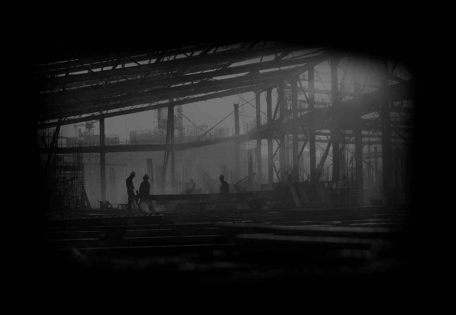 Obra en construcción de madrugada con siluetas de trabajadores entre la estructura de acero